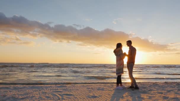 Guindaste tiro: Um casal amoroso de pé no pôr do sol junto ao mar, olhando um para o outro — Vídeo de Stock