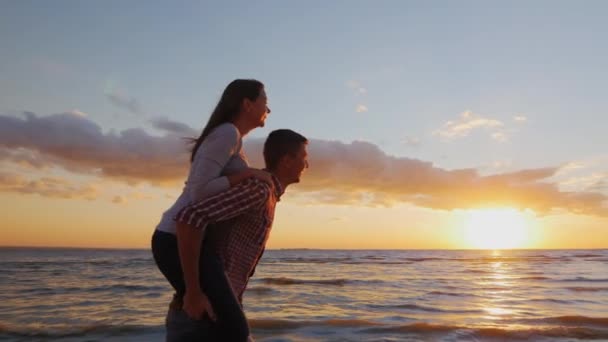 Milující dvojice se baví na pláži. Holka, co na něj jede, ukazuje ruku. Romantika, mládí a líbánky. Steadikam pomalý pohyb — Stock video
