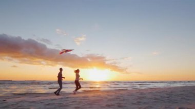 Young couple playing with a kite on the beach at sunset. Steradicam slow motion shot