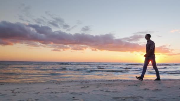 Jovem solitário caminhando ao longo da praia ao pôr do sol — Vídeo de Stock