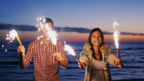 Young couple having fun with fireworks in the hands. Fireworks lit the pair laughing, having a good time. During sunset. Slow motion video — Stockvideo