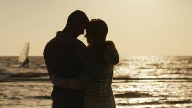 Gün batımında deniz kenarında sarılma sevgi dolu bir çift silüeti. Yelkenli uzakta yüzen