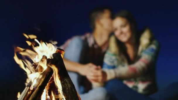 Romantisches Paar, das sich leise im brennenden Feuer unterhält. Schärfe am Feuer, ein junges Paar verschwimmt — Stockvideo