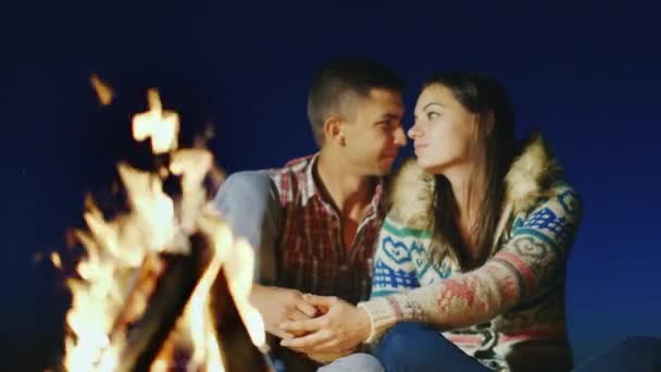 Um casal amoroso sentado ao lado do fogo, de mãos dadas, admirando o fogo — Vídeo de Stock