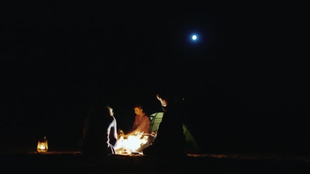 La compañía de amigos relajándose alrededor de la fogata, malvaviscos asados mujer en palos, un hombre cortando leña con un hacha — Vídeos de Stock