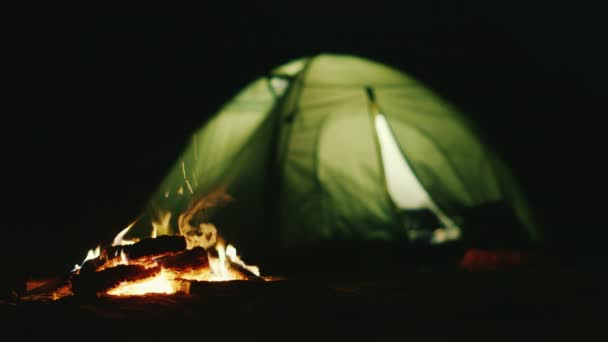 La tente dans laquelle la lumière brille près du feu brûle. Romance et détente dans la nature — Video