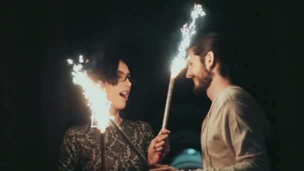 Um jovem com barba e uma mulher morena se divertindo com fogos de artifício nas mãos de — Vídeo de Stock