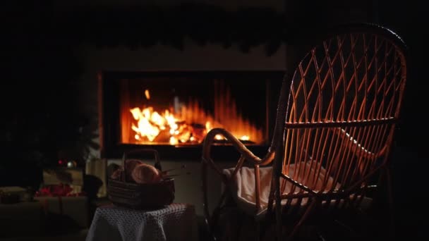 An empty rocking chair sways by the fireplace, next to a set for needlework. A place for winter holidays — Stock Video