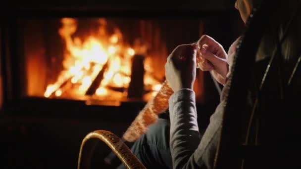 Женские руки с вязальными спицами - вяжет теплую одежду сидя у камина — стоковое видео