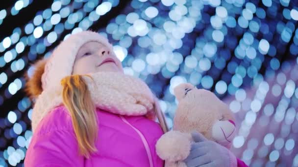 Et lille barn med et legetøj i hænderne beundrer juletræet – Stock-video