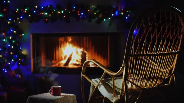 Cadeira de balanço junto à lareira decorada para o Natal, ao lado de uma xícara de chá quente com o qual há vapor — Vídeo de Stock