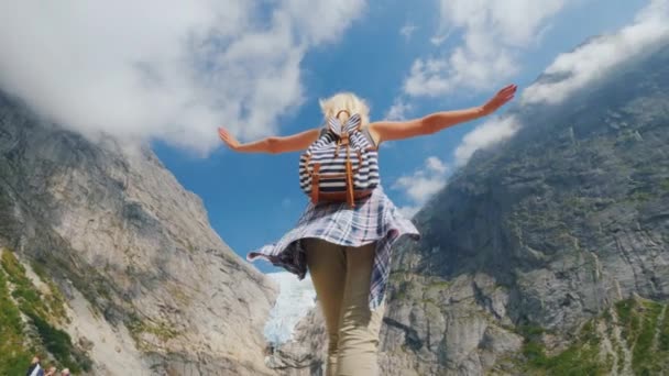 若い健康な女性は北欧の美しい自然を楽しんでいます。山頂に氷河がある山を背景に手を挙げて立つ — ストック動画