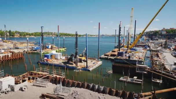 Stockholm, Sweden, July 2018: Large-scale construction on the river bed in Stockholm. On the platform there is construction equipment, pumping out of water. Against the background of the cityscape — Stock Video