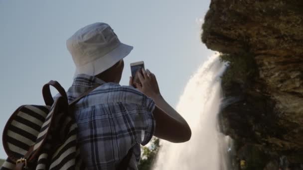 Uma silhueta de uma mulher tirando fotos de uma bela cachoeira na Noruega — Vídeo de Stock