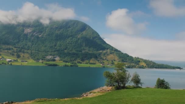 De oever van de fjord, de top van de bergen verdrinken in de wolken. Uitzicht vanuit het raam van het Noorse landschap. — Stockvideo