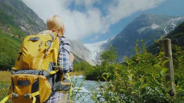Ένας ταξιδιώτης με ένα μεγάλο σακίδιο θαυμάζει το βουνό του ποταμού και παγετώνα στη Νορβηγία — Αρχείο Βίντεο