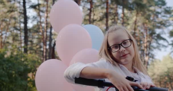 Retrato de una chica alegre al timón de un scooter y con globos en la parte posterior — Vídeo de stock