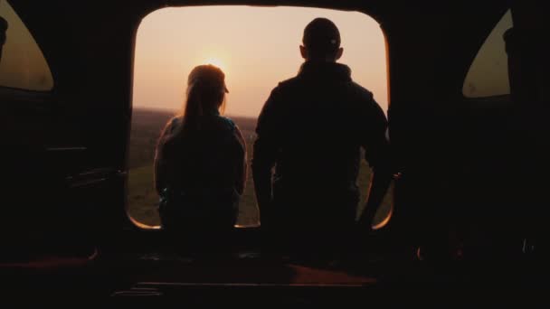 Bratr a sestra sedí bok po boku v kufru auta a dívají se na západ slunce na krásném místě — Stock video