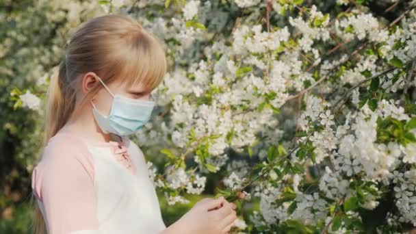 Грустное дитя в маске возле цветущих деревьев. Аллергия — стоковое видео