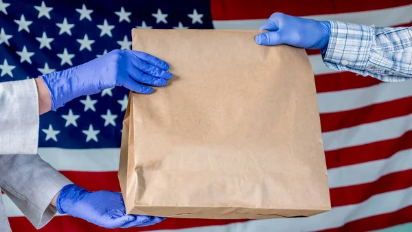 Bote in Handschuhen reicht das Paket vor dem Hintergrund der amerikanischen Flagge in die Hände des Empfängers — Stockfoto