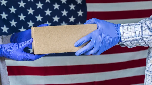 Bote in Handschuhen reicht das Paket vor dem Hintergrund der amerikanischen Flagge in die Hände des Empfängers — Stockfoto