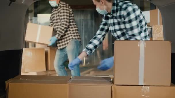 Transportadores en máscaras protectoras cargan cajas de cartón en el maletero de la furgoneta — Vídeos de Stock