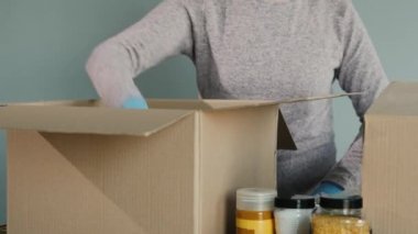 Koruyucu eldivenli bir kadın karton bir kutuya yiyecek koyar.