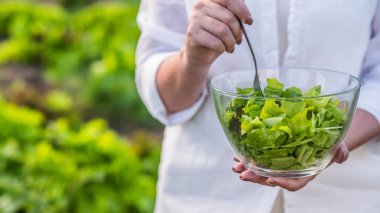 İnce kadın salata yiyor, büyüdüğü yatağın yanında duruyor.