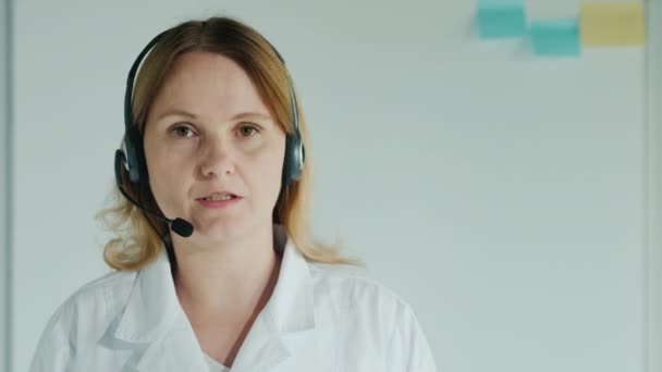 Žena doktor ve sluchátkách mluví s kamerou — Stock video