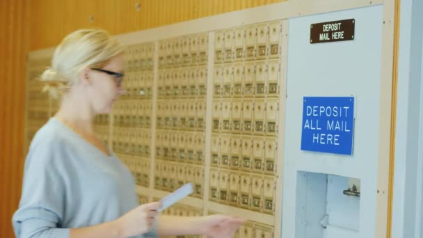 Молодая женщина в очках бросает несколько писем в почтовый ящик на почте — стоковое видео