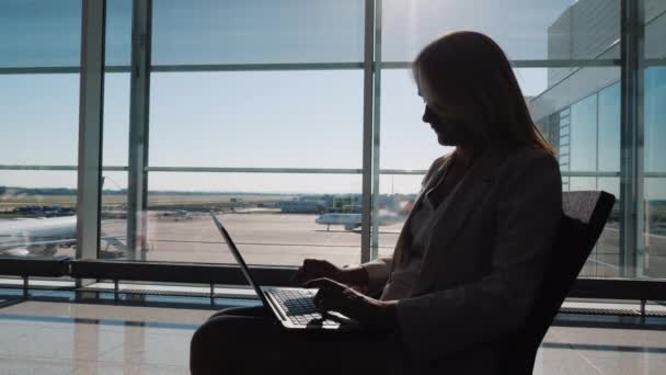 Jonge vrouw met laptop wachtend op haar vlucht op de luchthaven terminal. — Stockvideo