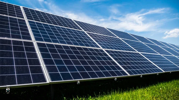 Paneles de plantas solares en un prado verde contra un cielo azul con nubes —  Fotos de Stock