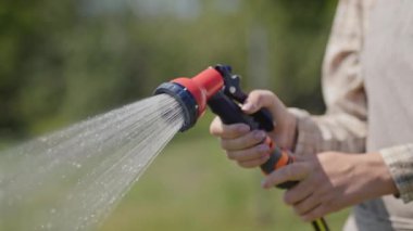 Kadın bahçıvan bahçe hortumundan bitki döküyor. Yan görünüm