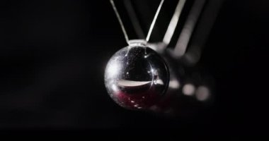 Metal toplar birbirine çarpıyor, bu da enerjinin korunumu kanununu gösteriyor. Newton sarkacı