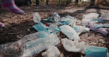 Çocuk ayakları botların içinde, tıbbi maskelerden yapılmış bir yığın çöpün yanından geçiyor. Çevre sorunları kavramı