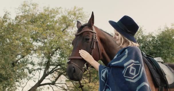 Портрет стильной женщины в шляпе и пончо возле лошади — стоковое видео