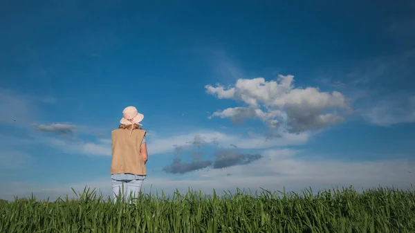 Uma mulher está em um prado verde contra um belo céu azul com nuvens — Fotografia de Stock