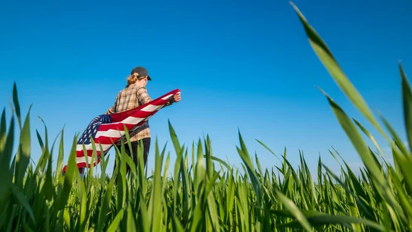 Eine Frau mit einer US-Flagge auf den Schultern steht auf einer malerischen grünen Wiese — Stockfoto