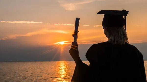 Il Bachelor con diploma in mano guarda il tramonto sul mare — Foto Stock