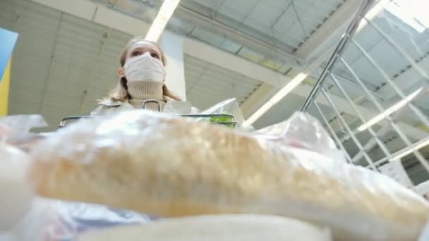 一个戴着防护面具的女人开着满载购物车穿过超市 — 图库视频影像