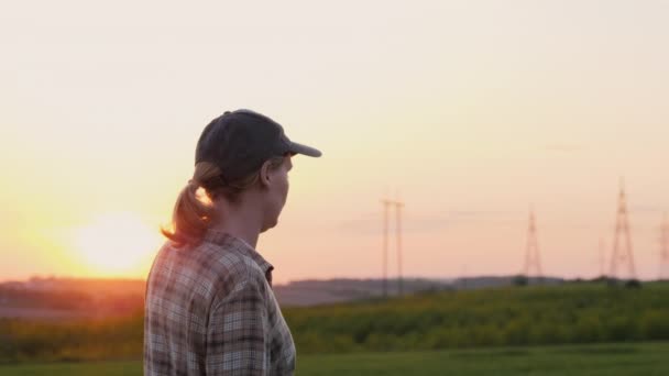 Vista lateral: Uma agricultora caminha por um campo pitoresco ao pôr do sol — Vídeo de Stock