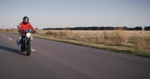 Motociclista en una chaqueta roja monta en un camino de campo — Vídeos de Stock