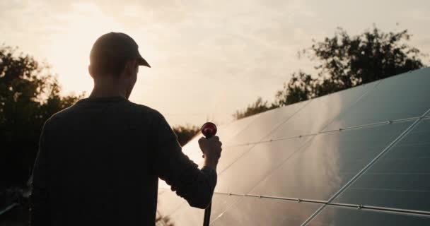 Güneş enerjisi santrali panelini yıkayan bir adamın silüeti. — Stok video