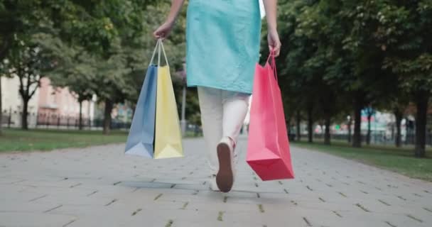 Młoda kobieta niesie torby na zakupy ze sklepów z modą, w ramce widać tylko jej stopy i torby — Wideo stockowe