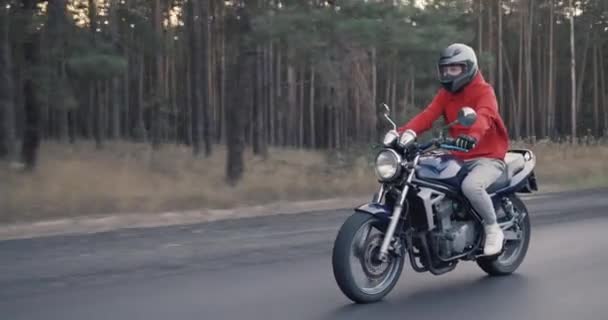 Jonge motorrijder rijdt snel langs de weg langs het bos — Stockvideo