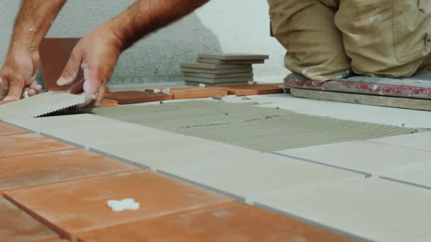Строитель кладет керамическую плитку на пол на открытой веранде. — стоковое видео