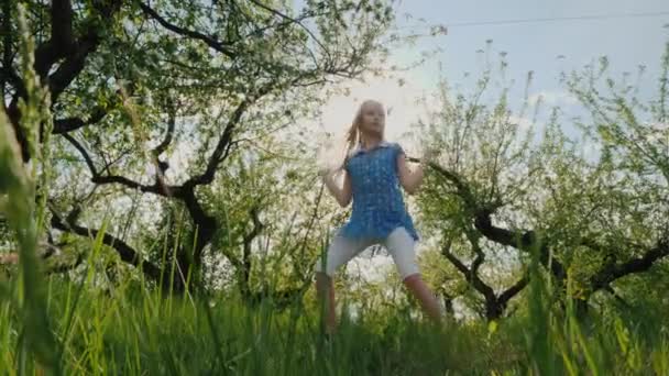 Zabawna dziewczyna tańczy w jabłkowym sadzie w słońcu — Wideo stockowe