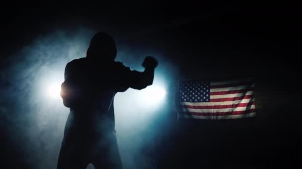 La silhouette d'un combattant cool, s'entraîne dans le hall sous les projecteurs, en arrière-plan du drapeau américain — Video