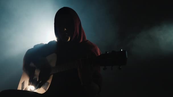 A young man plays the guitar, sits on stage in a fog — Stock Video