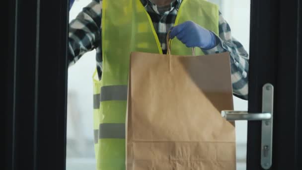 Der männliche Kurier bringt ein Paket mit Lebensmitteln zur Bestellungstür. Hes trägt Schutzhandschuhe. — Stockvideo